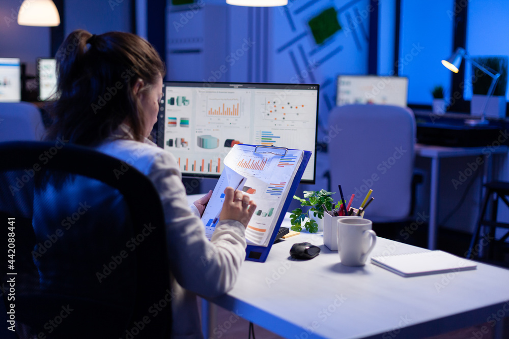 Poster freelancer woman comparing graphics from clipboard with grafics from computer at business office. ti