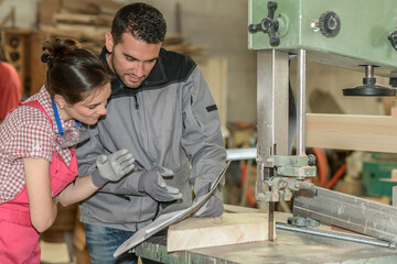 Female trainee and male mentor cutting a piece of wood  in workshop