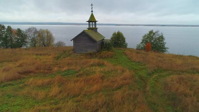 Flight forward to cinematic Karelia wooden small Chapel St. George Victorious old traditional temple church on shore of Onega lake. Cross roof overgrown with moss. Russia historical landmark. Cloudy 