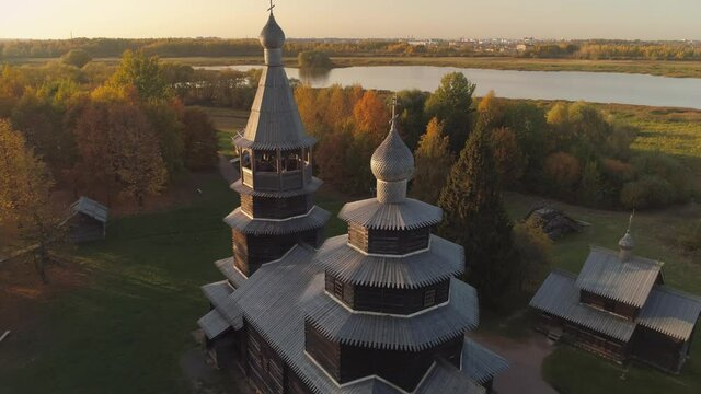 Flight above beautiful Russia traditional wooden church Vitoslavlitsy Veliky Novgorod authentic tample at orange sunset dome cross. Chapel on lake coast. Orthodox religion traditions heritage. Horizon