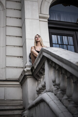 Attractive young blonde female sitting on the stone handrailing of a staircase
