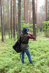 Young woman with black backpack holding the hat  while exploring  local nature. Hiking and travelling in forest concept