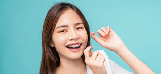 Smiling Asian woman cleaning braces on teeth with dental floss on blue background, Concept oral...