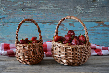 Fototapeta na wymiar Two wicker baskets with ripe straberries, checkered napkin on old paint wooden background