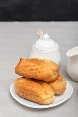 Homemade eclairs on a plate and next to jar with sugar. Profiteroles on saucer without glaze. Baking for tea