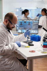 Scientist doing genetic experiment using blood sample on micropipette dropped on petri dish. Team...