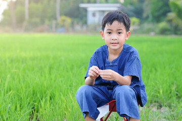 Asian boy wear traditional farmer costume sitting at green rice farm.