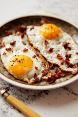 Two fresh fried eggs with crunchy crisp bacon served on rustic plate
