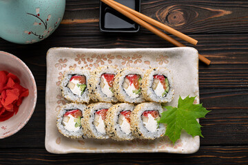 Set of sushi rolls with cream cheese, rice and salmon on a board decorated with ginger on a dark wooden background. Japanese cuisine. Food photo