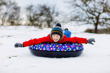 Active school boy sliding down the hill on snow tube. Cute happy child having fun outdoors in...