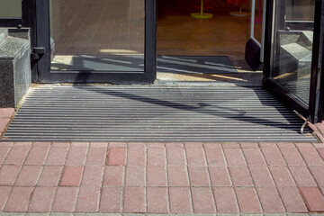 entrance to the store from a pedestrian sidewalk from a plink on a foot mat through a glass door,...