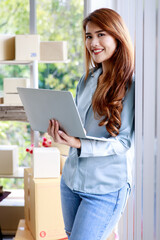 in office of delivery service business, beautiful young woman standing with laptop and happily smile as she satisfying good progress of her commercial job