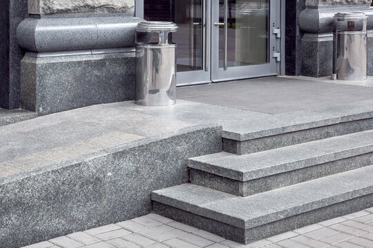 granite gray porch step with a foot mat at the entrance to the central door made of tempered glass architecture market style with ramp and trash can, nobody.