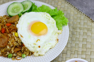 Nasi Goreng or Fried Rice, one of Indonesian popular food, topping with sunny side up egg, cucumber slices, lettuce and crackers. Top view, copy space for text.