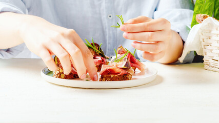 Female hand holds rosmarinon bruschetta with raw ham and fresh fig.