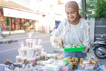 A beautiful girl in veil holding a plastic tray chooses various types of fritters to buy at a roadside stall
