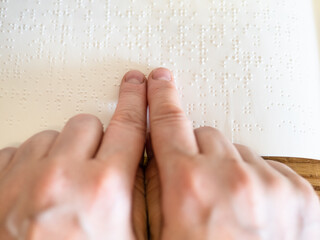 point-of-view reading book with braille by fingertips closeup on wooded table