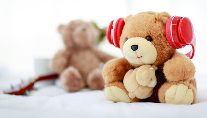in home bedroom, brown lovely fluffy teddy bear toy creatively wearing red earphone and sit on bed near guitar as lovely doll for enjoy music playing on delight celebration holiday