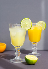 a couple of vintage glasses with a cold citrus drink or lemonade or alcoholic cocktail on gray background, two vintage goblets among cutting orange and lime, minimalism