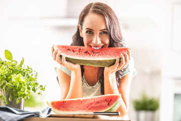 Good-looking girl bites into the the quarter of a watermelon in the kitchen, smiling
