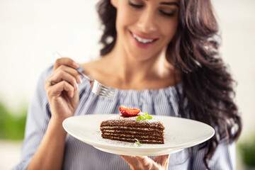 Layered brown adn white cake with strawberry and mint leaf on top held by a woman with a fork