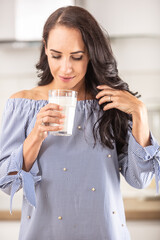 Woman smiles and looks into her glass of milk in the hand standing in the kitchen