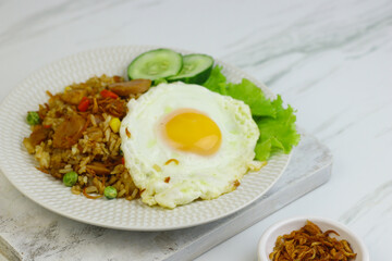 Nasi Goreng or Fried Rice, one of Indonesian popular food, topping with sunny side up egg, cucumber slices, lettuce and crackers. Top view, copy space for text.