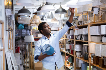 African American male shopper looking for table lamp and pendant light in household goods store. Home improvement concept
