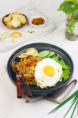 Nasi Goreng or Fried Rice, one of Indonesian popular food, topping with sunny side up egg, cucumber slices, lettuce and crackers. Top view, copy space for text.