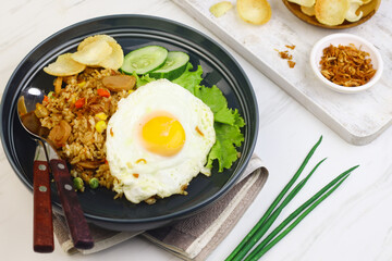 Nasi Goreng or Fried Rice, one of Indonesian popular food, topping with sunny side up egg, cucumber slices, lettuce and crackers. Top view, copy space for text.