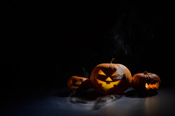 Pumpkins with carved grimaces and candles inside in the dark for halloween. Jack o latern in smoke.