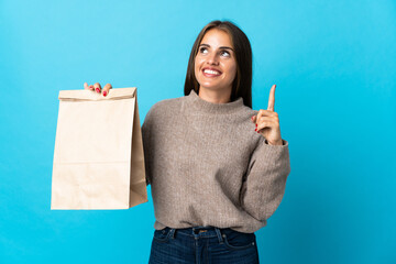 Woman taking a bag of takeaway food isolated on blue background pointing up a great idea