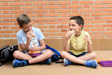 Two school boys happily eating a sandwich during school recess.