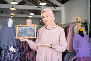 close up of a girl in a veil hold a blackboard with finger pointing gesture while standing inside a boutique shop