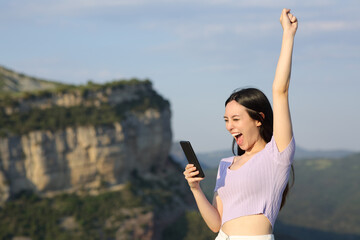 Excited asian woman checking phone in the mountain