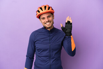 Young Brazilian cyclist man isolated on purple background saluting with hand with happy expression - obrazy, fototapety, plakaty