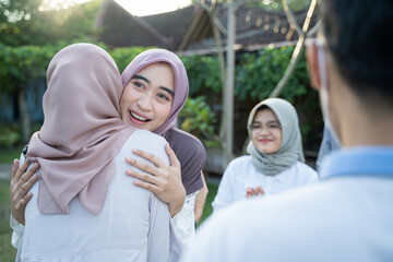 a woman wearing a headscarf hugs a veiled woman during a gathering in the yard
