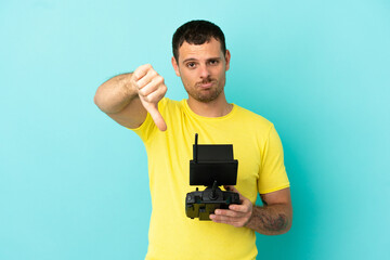Fototapeta na wymiar Brazilian man holding a drone remote control over isolated blue background showing thumb down with negative expression
