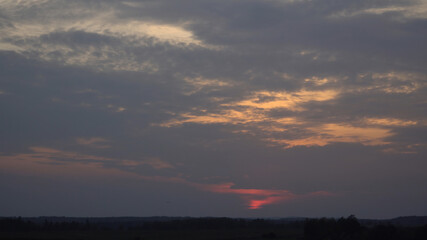 Evening the colorful cloudy sky at the sunset time. The picturesque landscape with a visible horizon line and woods silhouettes.