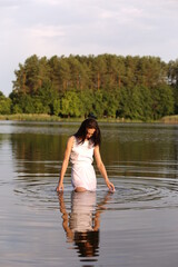 Beautiful brunette woman in white dress in the lake