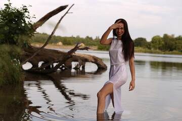 Beautiful brunette woman in white dress standing on a snag in the lake