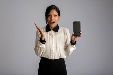 Young beautiful woman holding and showing blank screen smartphone or mobile or tablet phone on a gray background.