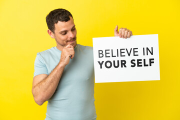 Brazilian man over isolated purple background holding a placard with text Believe In Your Self and thinking