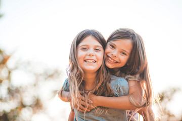 Portrait of two little smiling girls playing in nature. Little girl carrying her friend.