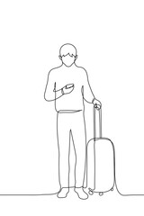 young man is holding a phone in which he is looking, in his other hand a suitcase on wheels - one line drawing vector. a passenger has arrived or is waiting in line for boarding