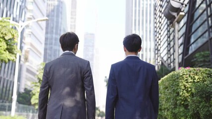 rear view of two asian business men walking talking on street in downtown financial district of modern city - Powered by Adobe