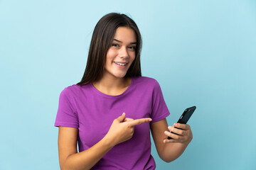 Teenager girl isolated on pink background using mobile phone and pointing it