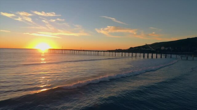 Aerial: Waves crashing at sunset at the beach. Pismo Beach
