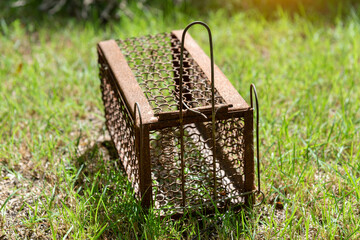 Empty  old steel cage for mousetrap placed on  green grass. The rat trap is stil