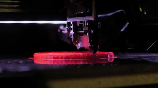 Three dimensional printer making red flat physical plastic 3D model at modern futuristic exhibition - close up. Additive technology, equipment, prototype, manufacturing and production concept
